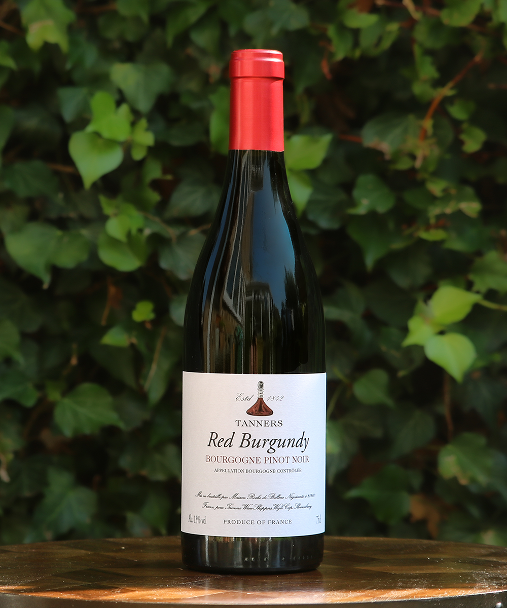 Bottle of Tanners Red Burgundy wine on a wooden surface with a green leafy background