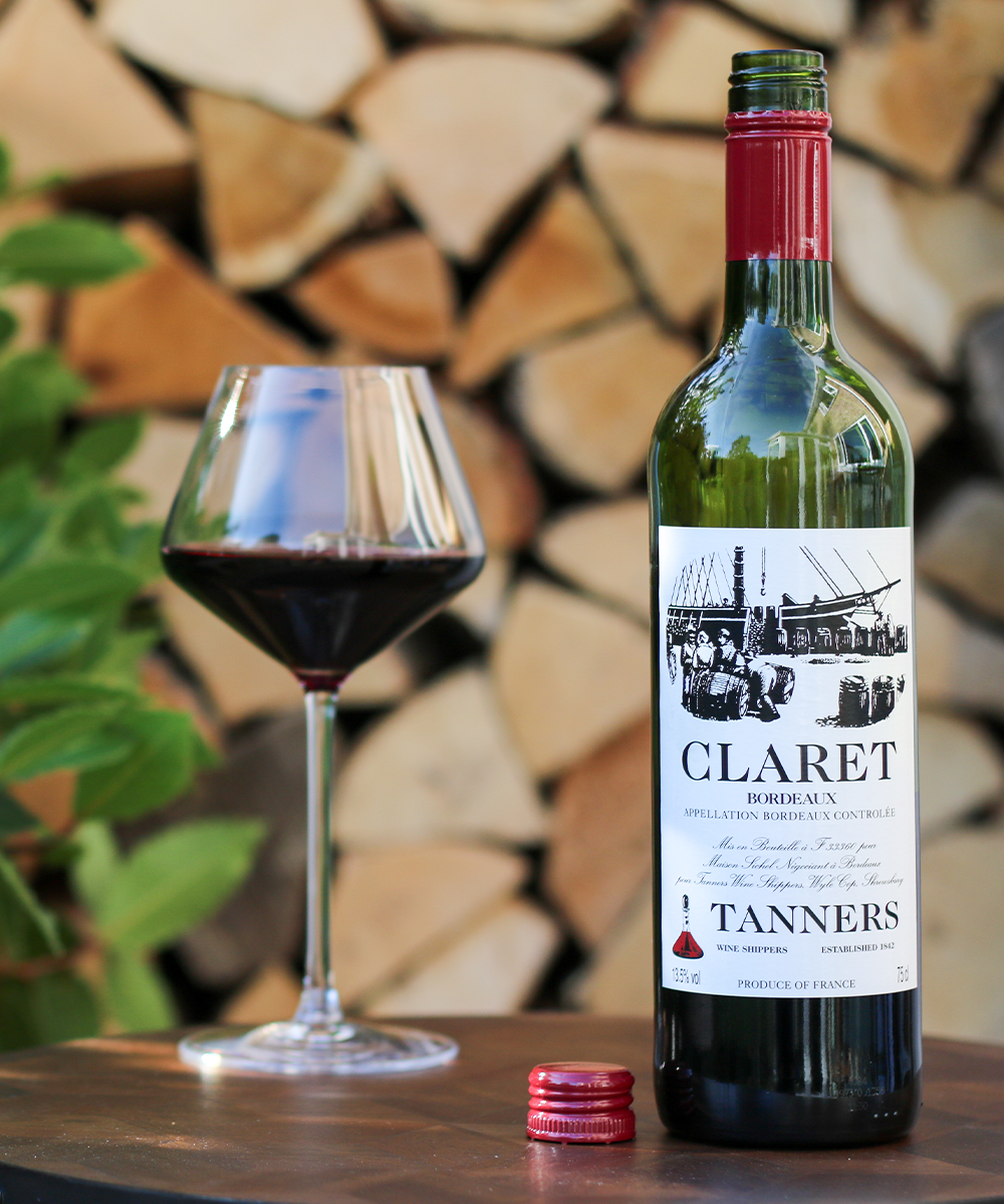 Bottle of Claret wine from Tanners with a glass of wine on a wooden surface.