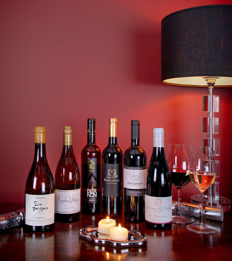 Collection of wine bottles on a table with a red wall and lamp in the background
