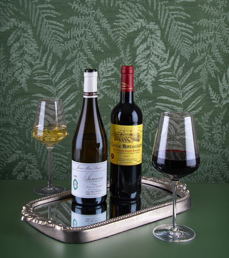 Two wine bottles and two glasses on a silver tray with a green leafy background