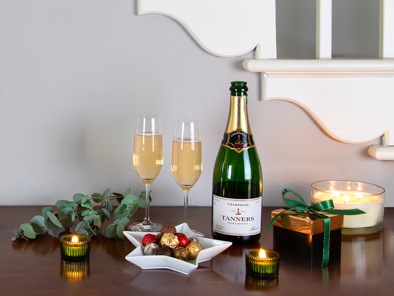 Bottle of Tanners champagne with two glasses, a small gift box, and decorative items on a table.
