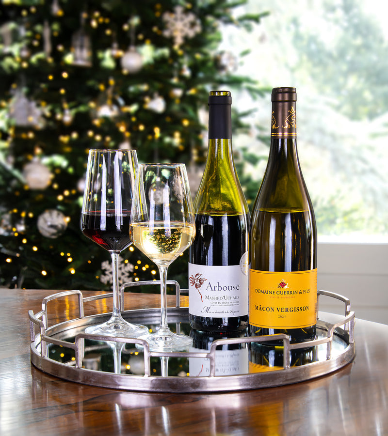 Two wine bottles and two glasses on a tray with a Christmas tree in the background