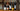 Five wine bottles lined up on a wooden table with pinecones in front of rustic wooden beams. The bottles include wines from Tanners, Laurent Perrier, and Domaine Guerrin & Fils.