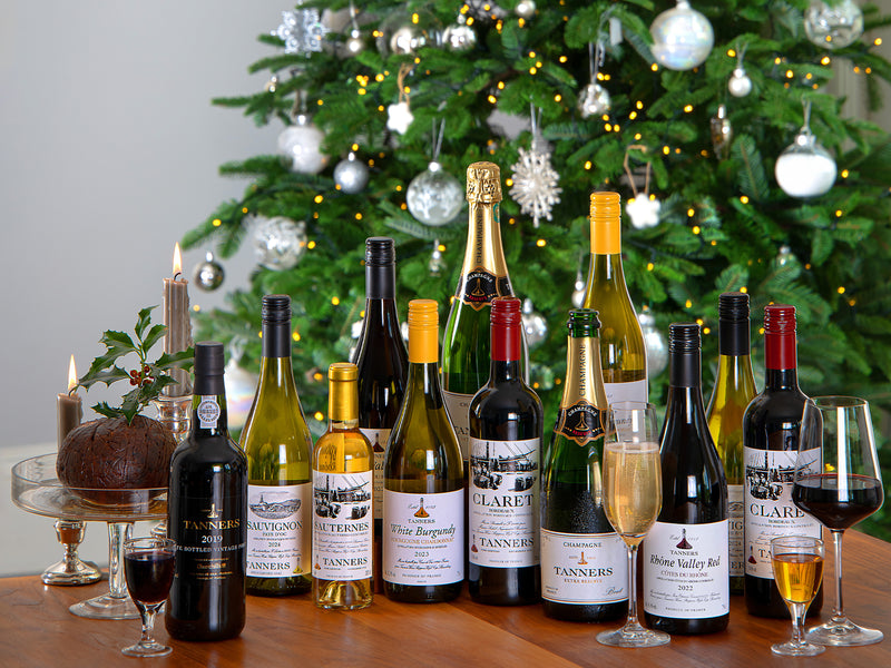 Assorted wine bottles on a table with a decorated Christmas tree in the background