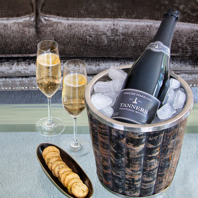 Bottle of Tanners English Sparkling Wine in an ice bucket with two glasse on a table.