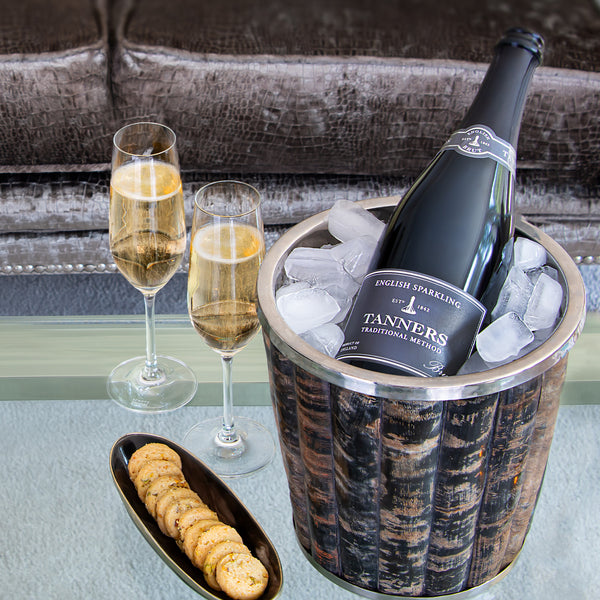 Bottle of Tanners English Sparkling Wine in an ice bucket with two glasse on a table.