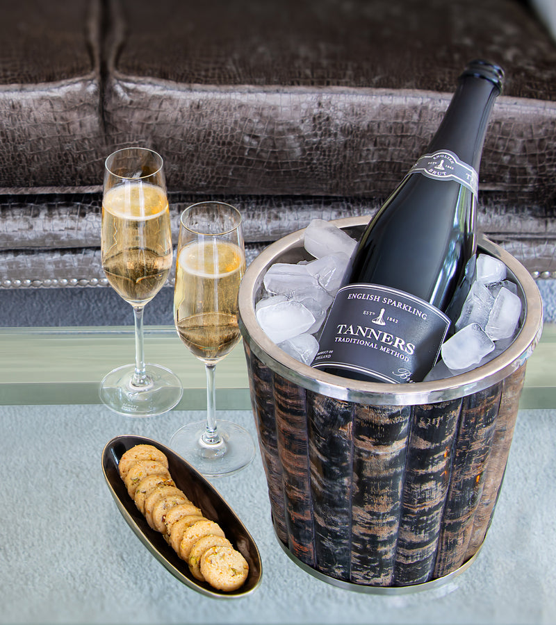 Bottle of Tanners English Sparkling Wine in an ice bucket with two glasse on a table.