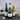Three wine bottles on a dark surface with glasses and decorative items, against a gray textured background.
