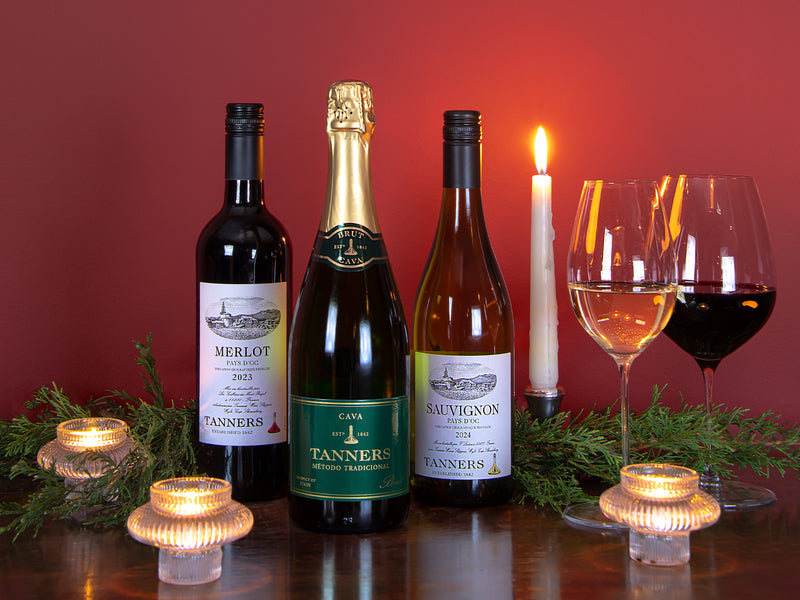 Wine bottles and glasses on a table with candles and greenery against a red background