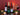 Wine bottles and glasses on a table with candles and greenery against a red background