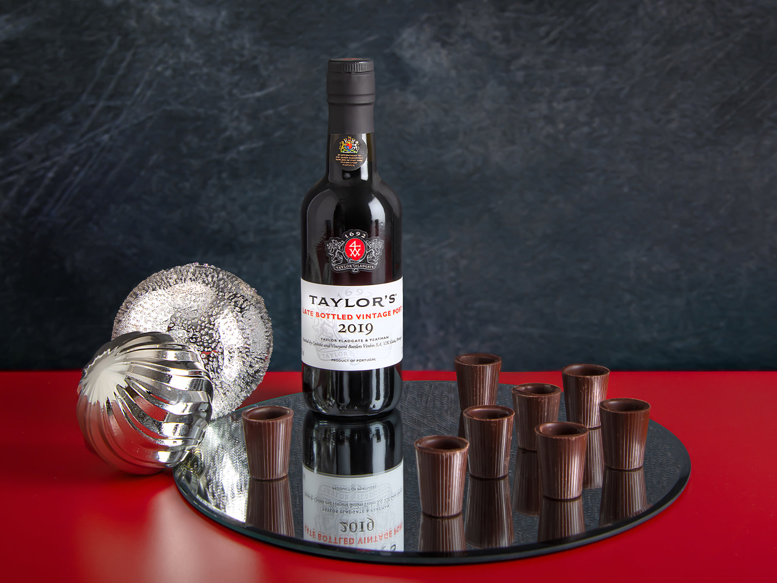 Bottle of Taylor's Port wine with chocolate cups on a reflective surface against a dark background