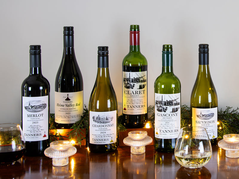 Collection of wine bottles with labels on a reflective surface with candles in the background