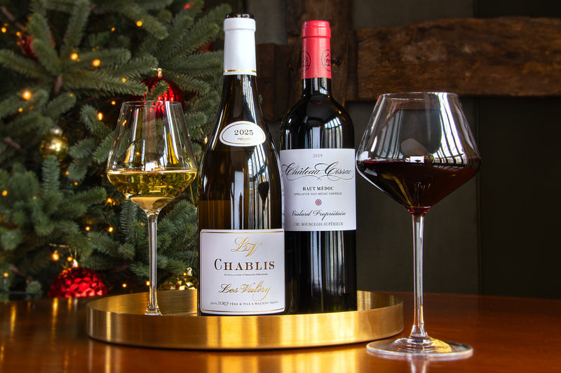 Two wine bottles and two wine glasses arranged on a gold tray in front of a decorated Christmas tree. The center bottle is a lovely bottle of Chablis, Les Valéry and the right bottle a brilliant Château Cissac, Haut-Médoc.