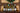 A group of wine bottles arranged on a wooden shelf against a rustic wood panel background, with decorative candles and greenery visible. Bottles include a Hay Stack Chardonnay, Bleu d'Alba Albariño, Pask Chardonnay, La Cabane, and a Campotino.
