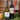 Two bottles of Tanners wine, including a New Zealand Sauvignon Blanc white wine bottle and an Argentinian Malbec red wine bottle, displayed on a gold tray with a filled wine glass, greenery, and a candle against a wooden paneled wall.