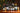A group of assorted wine bottles arranged on a wooden table in front of a decorated Christmas tree and rustic wooden wall. Notable brands include La Cabane, 770 Miles, PASK, Cucao and Campotino.
