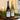 Two bottles of Chevallier Bernard wine and a filled wine glass on a decorative tray, styled with greenery and candles near a window.