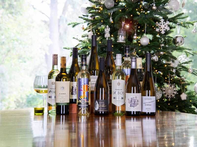 Assorted wine bottles on a table with a Christmas tree in the background